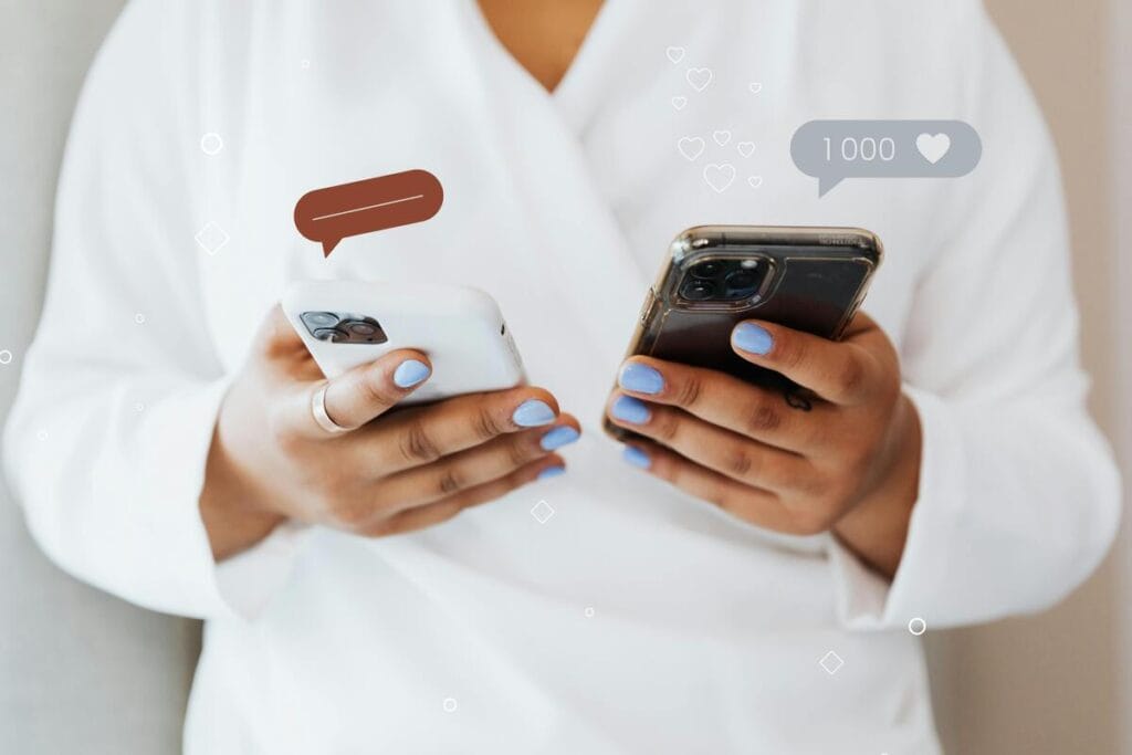 Manos sosteniendo dos smartphones con iconos de burbujas de chat y likes, simbolizando el UGC y la prueba social.