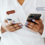 Manos sosteniendo dos smartphones con iconos de burbujas de chat y likes, simbolizando el UGC y la prueba social.